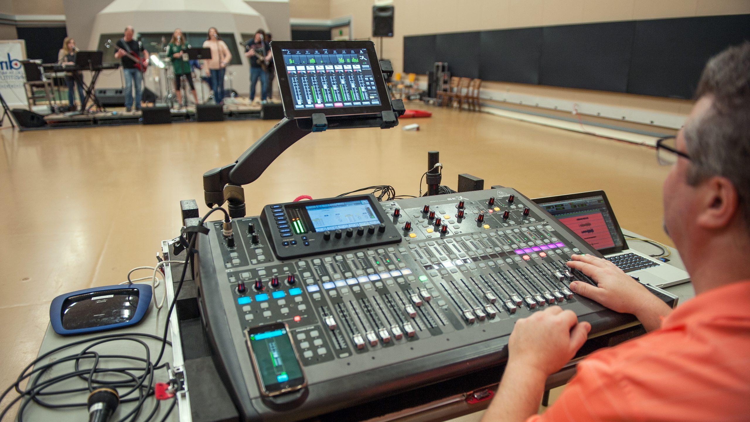 Man controlling digital sound board for a 6-piece band performing on a stage.